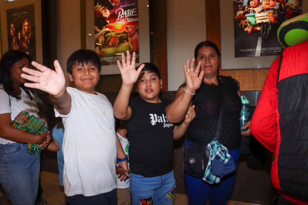 Niños del Albergue Frieda Heller saludando junto a su mamá, listos para entrar a la sala del cine.